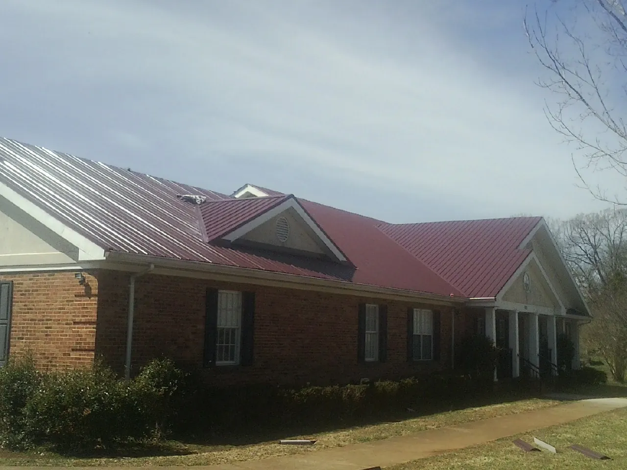 Red metal roof with gabled entries on a long brick building, from a Hail Damage Roof Repair job in Emmitsburg