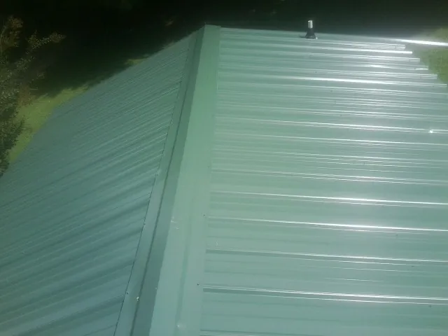 New green metal panels meeting at the ridge of a roof — Flat Roof Repair work by our crew in Emmitsburg