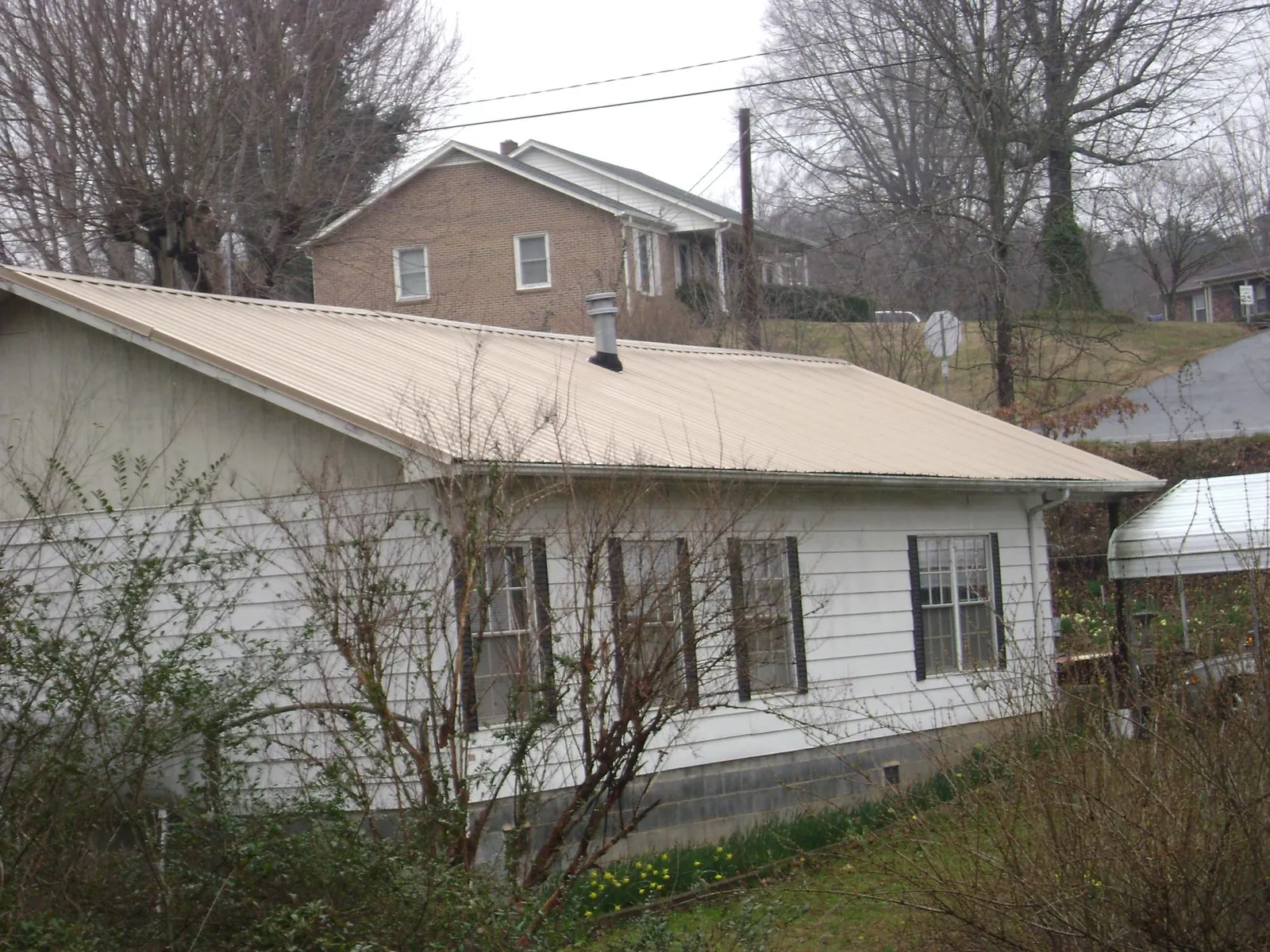 Tan metal roof on a white sided house set into a hillside — Commercial Roofing by Roofing Brothers in Emmitsburg